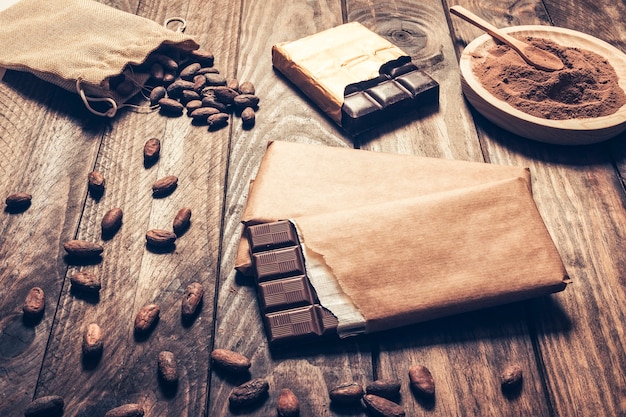 Kostenloses Foto dunkle schokoriegel mit kakaobohnen auf hölzernem hintergrund