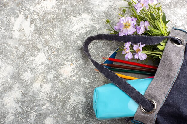 Dunkle Tasche der Draufsicht mit Heften und Blumen auf weißer Oberfläche