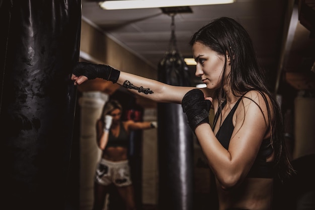 Dunkles Foto einer jungen hübschen Frau in einem dunklen Fitnessstudio, das mit einem Boxsack trainiert.