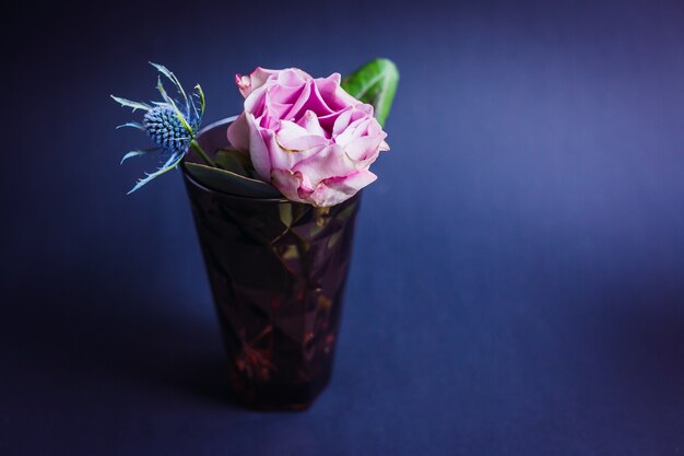 Dunkles violettes Glas mit rosa Rose und blauem Kegel
