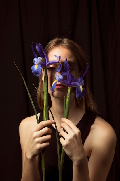 Durchdachte Frau, die blaue Blumen am Gesicht hält