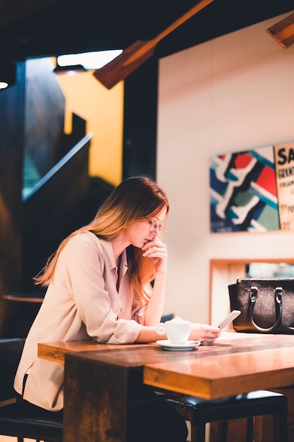 Durchdachte Frau, die Smartphone im Restaurant verwendet