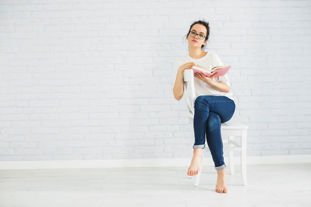 Durchdachte Frau mit Buch auf Stuhl