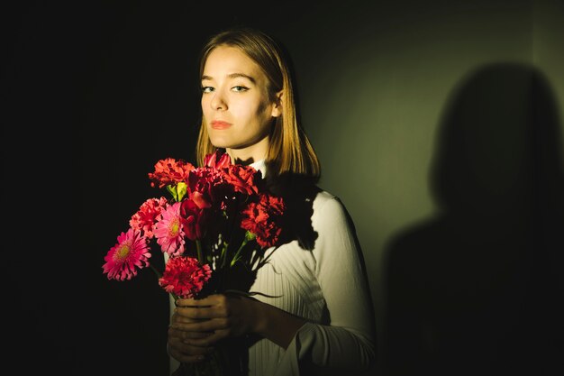 Durchdachte junge Frau mit hellem Blumenblumenstrauß