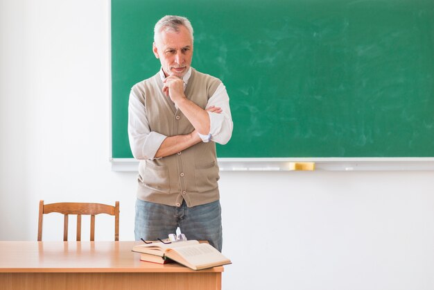 Durchdachter älterer Professor, der gegen grüne Tafel steht