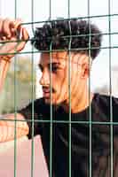 Kostenloses Foto durchdachter ethnischer junger mann hinter zaun