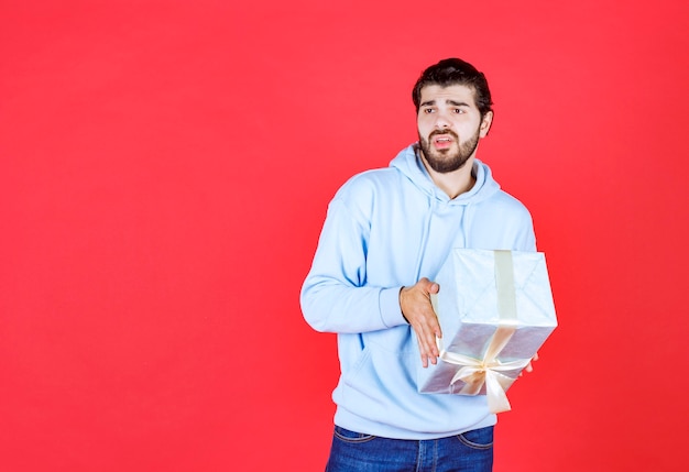 Durchdachter gutaussehender Mann, der verpackte Geschenkbox hält holding