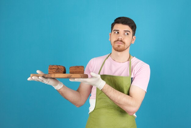 Durchdachter junger gutaussehender Mann, der Kuchenscheiben hält und wegschaut.