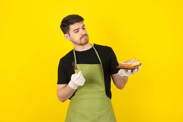 Durchdachter junger Mann, der Kuchenscheibe auf einem Gelb betrachtet.