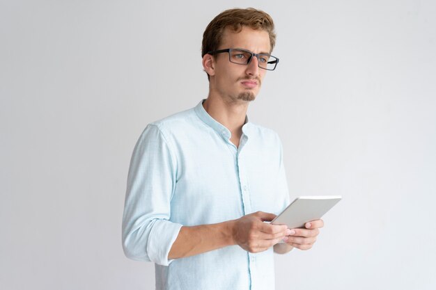 Durchdachter junger Mann, der Tablet-Computer hält