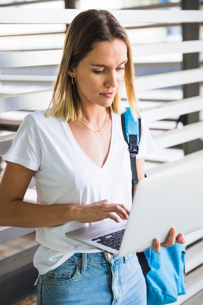 Durchsuchende Laptop der reizenden Frau nahe Wand