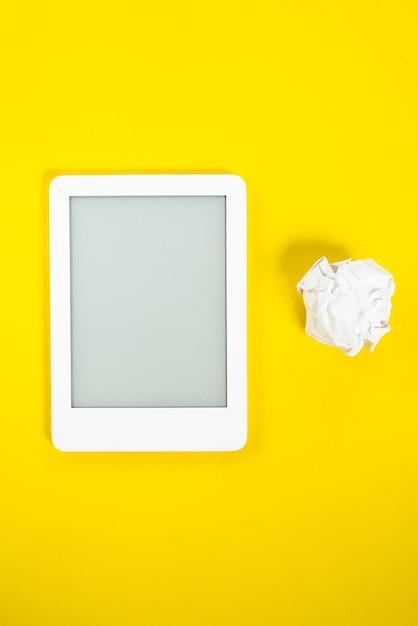 Kostenloses Foto ebook-leser über gelbem hintergrund mit papierkugel daneben