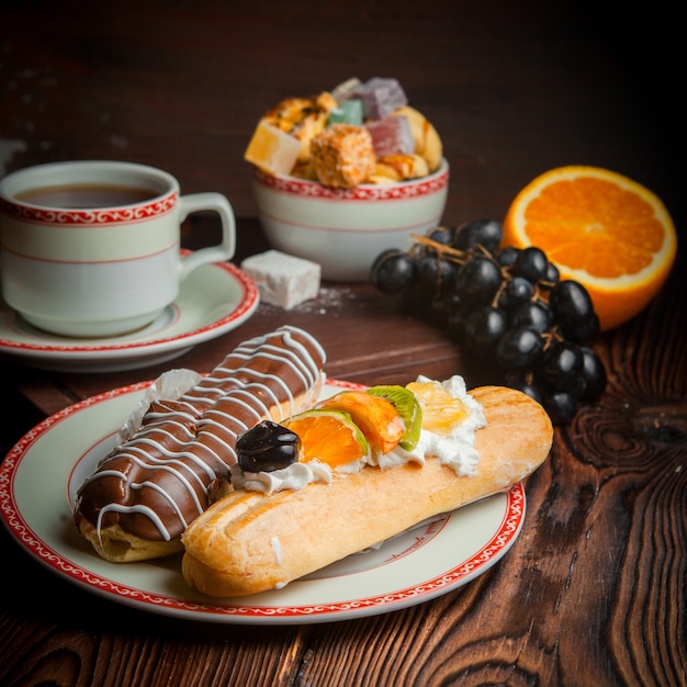 Eclair mit Traube und Orange und Tasse Tee in Teller