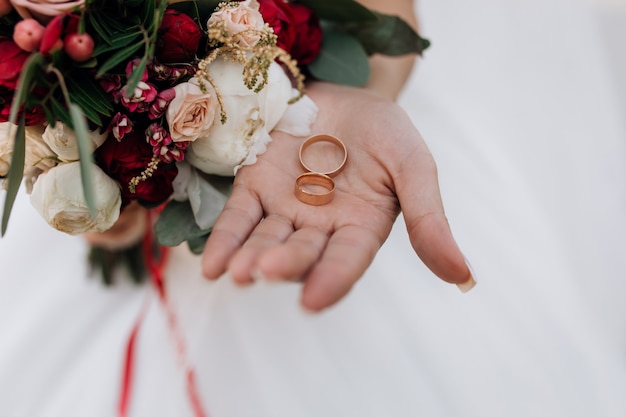 Eheringe an der Hand der Frau, Hochzeitsstrauß von roten und weißen Blumen, Hochzeitsdetails
