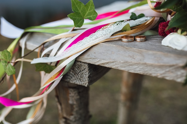 Eheringe liegen auf dem Holztisch nahe einem Blumenstrauß mit vielen Bändern