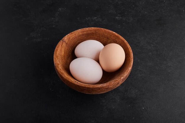 Eier in einer hölzernen Tasse auf Schwarzraum.