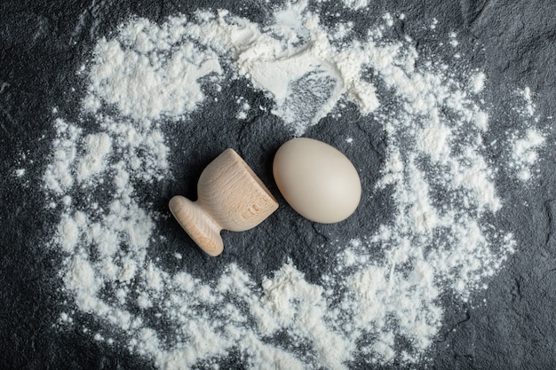 Eierbecher und rohes Ei auf mehligem Hintergrund.