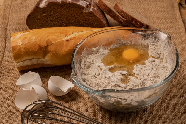 Eigelb auf dem Mehl. Eierschalen, Baguette- und Roggenbrotscheiben und Handmixer auf einem Stück Leinwand.