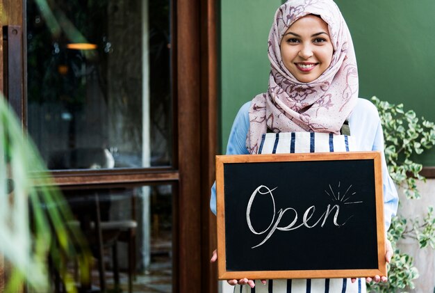 Eigentümer der islamischen Frau des kleinen Geschäfts, der Tafel mit dem Lächeln hält