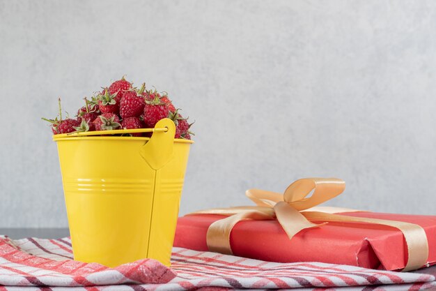 Eimer mit frischen Erdbeeren und Geschenkbox auf Marmoroberfläche. Hochwertiges Foto