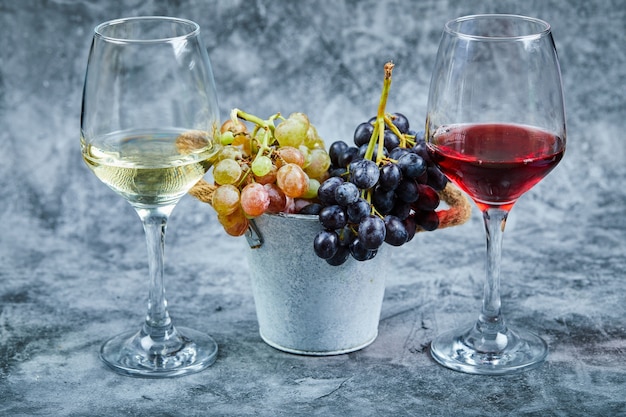 Eimer mit Trauben und Gläsern Wein auf Marmorhintergrund
