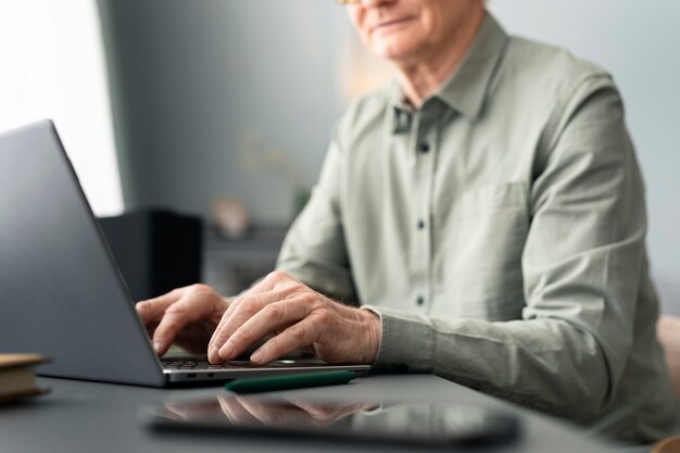 Ein älterer Mann benutzt einen Laptop, der am Schreibtisch im Wohnzimmer sitzt