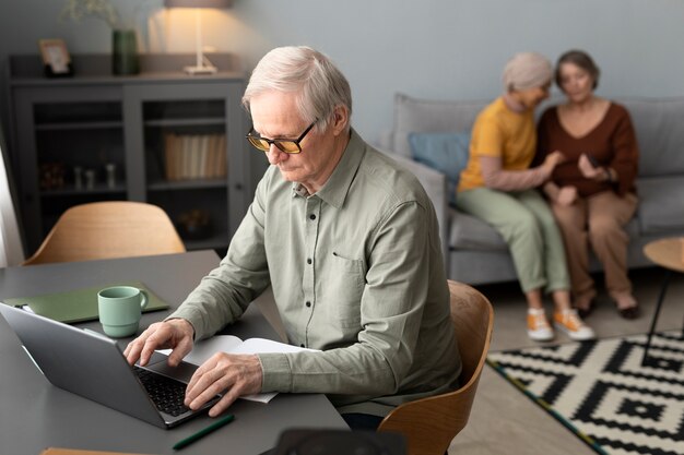 Ein älterer Mann benutzt einen Laptop, der am Schreibtisch im Wohnzimmer sitzt