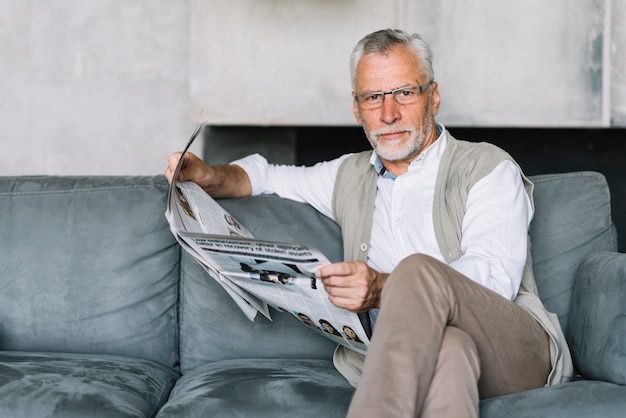 Ein älterer Mann, der auf Sofa liest Zeitung sitzt