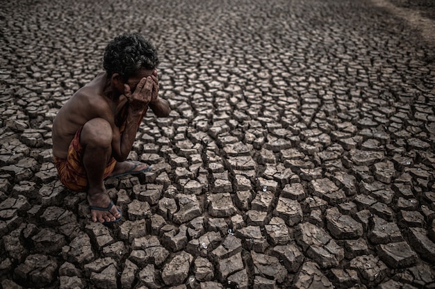 Ein älterer Mann saß mit gebeugten Knien auf trockenem Boden und schloss die Hände vor dem Gesicht, die globale Erwärmung