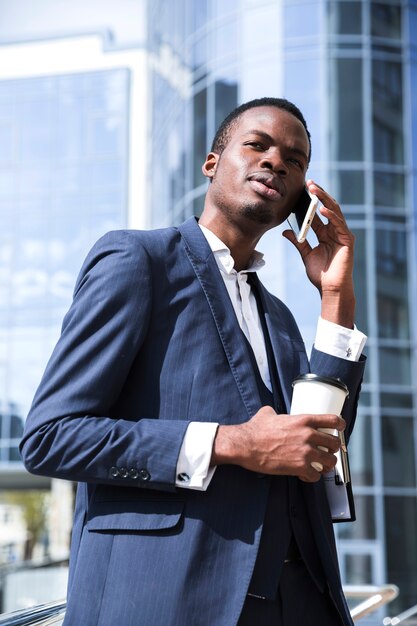 Ein afrikanischer Geschäftsmann, der am Handy hält Wegwerfkaffeetasse spricht