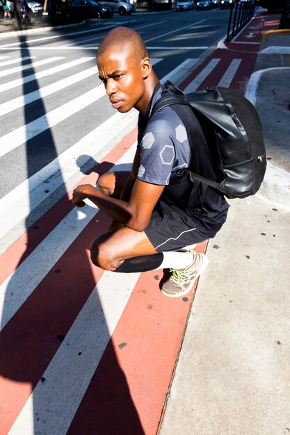 Ein afrikanischer junger männlicher Athlet, der auf dem Straßenrand sich duckt, der weg schaut