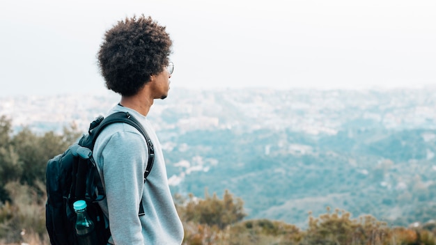 Ein afrikanischer junger männlicher Wanderer mit seinem Rucksack, der Ansicht betrachtet