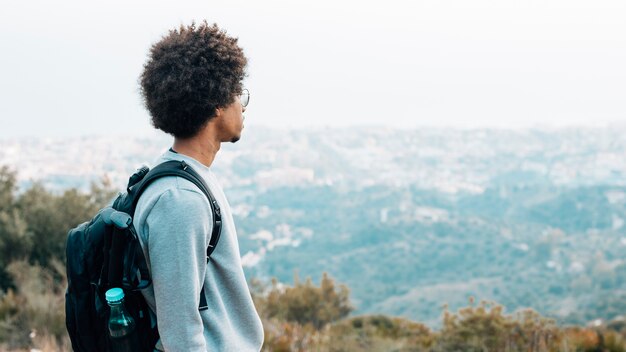 Ein afrikanischer junger männlicher Wanderer mit seinem Rucksack, der Ansicht betrachtet