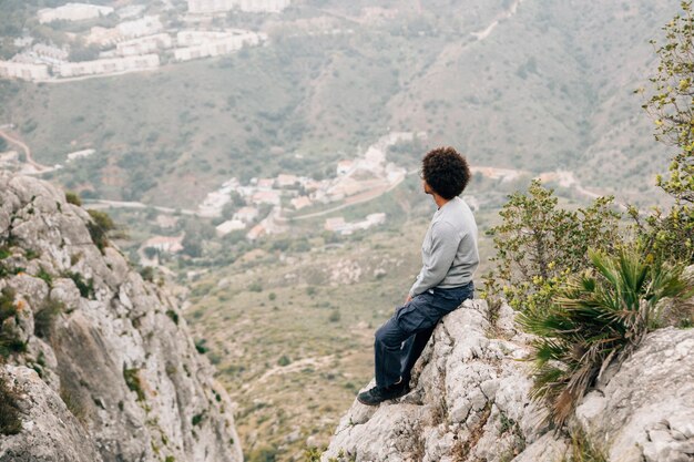 Ein afrikanischer junger Mann, der auf dem Felsen übersieht den Bergblick sitzt