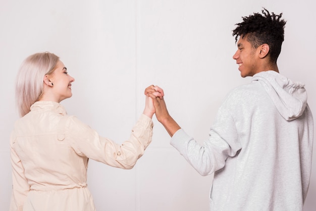 Ein afrikanischer junger Mann und eine blonde Frau, welche die Hände stehen gegen weißen Hintergrund anhalten