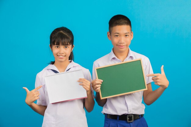 Ein asiatischer Student, der ein Notizbuch hält, und ein asiatischer männlicher Student, der ein grünes Brett auf einem Blau hält.