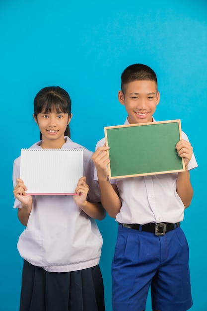 Ein asiatischer Student, der ein Notizbuch hält, und ein asiatischer männlicher Student, der ein grünes Brett auf einem Blau hält.