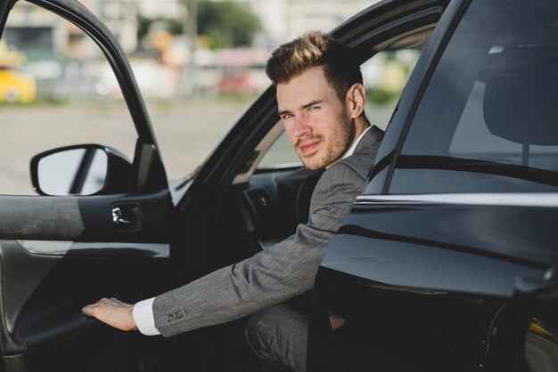 Ein attraktiver junger Geschäftsmann, der heraus vom Auto schaut