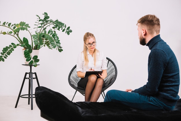 Ein attraktiver weiblicher Psychologe, der auf den männlichen Patienten sitzt auf Couch hört