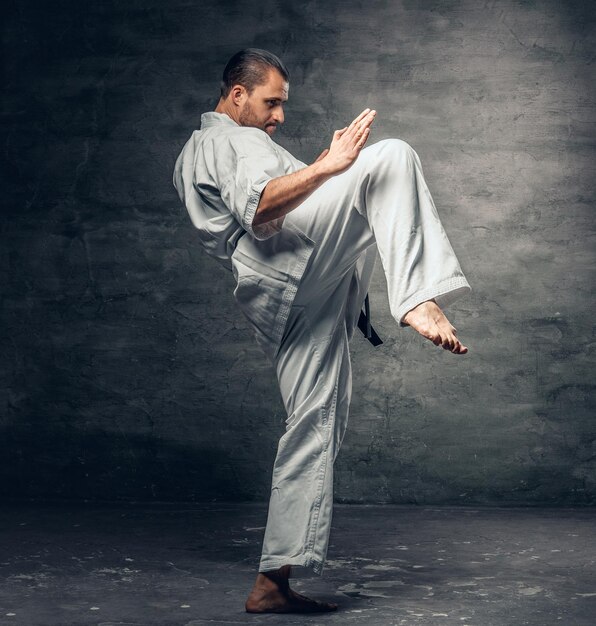 Ein bärtiger Karatekämpfer mit einem Tattoo auf seinem Arm, gekleidet in einen weißen Kimono.