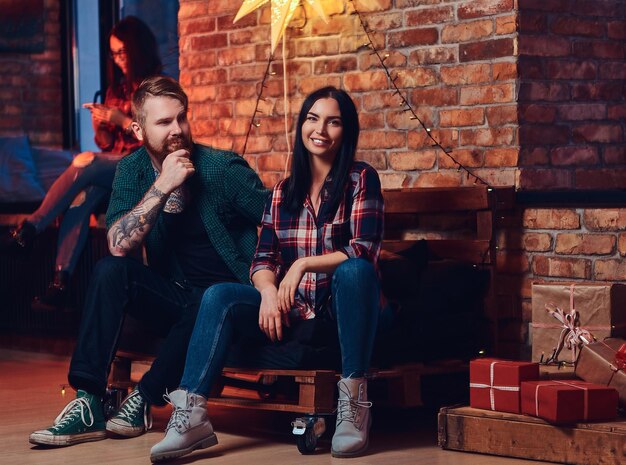 Ein bärtiger Mann und zwei brünette Frauen Weihnachtsfeier in einem Raum mit Loft-Interieur.