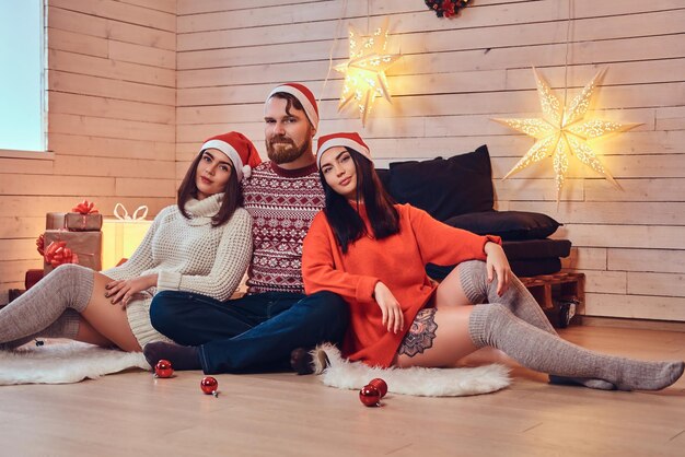 Ein bärtiger Mann und zwei brünette Frauen Weihnachtsfeier über weißer Holzwand.