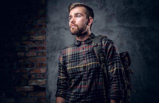 Ein bärtiger Reisender, der in einem Fleecehemd mit Rucksack gekleidet ist und auf grauem Hintergrund posiert.