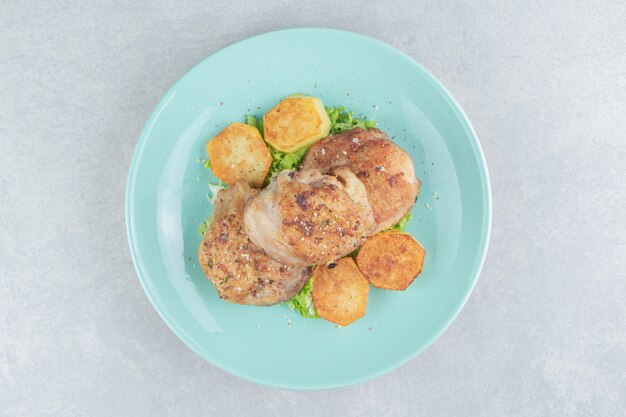 Ein blauer Fleischteller mit Bratkartoffeln und Salat.