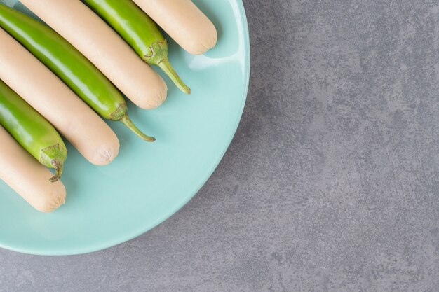 Ein blauer Teller mit gekochten Würstchen mit Chilischoten.