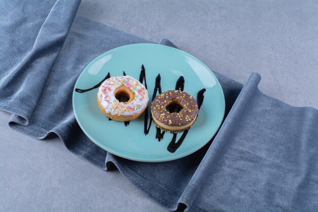 Ein blauer Teller mit zwei süßen Donuts mit bunten Streuseln.