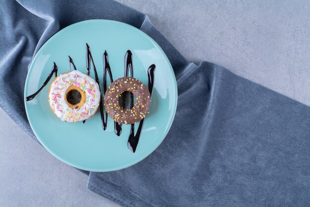 Ein blauer Teller mit zwei süßen Donuts mit bunten Streuseln.