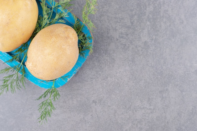 Ein blaues Holzbrett aus ungekochten Kartoffeln mit frischem Dill.