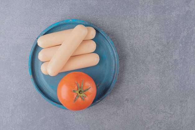 Ein blaues Holzbrett gekochter Würste mit roter Tomate.