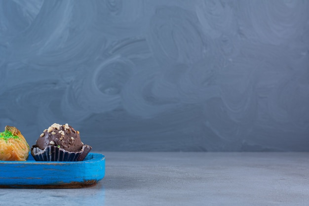 Ein blaues Holzbrett mit zwei Schokoladen-Cupcakes und Baklawa.